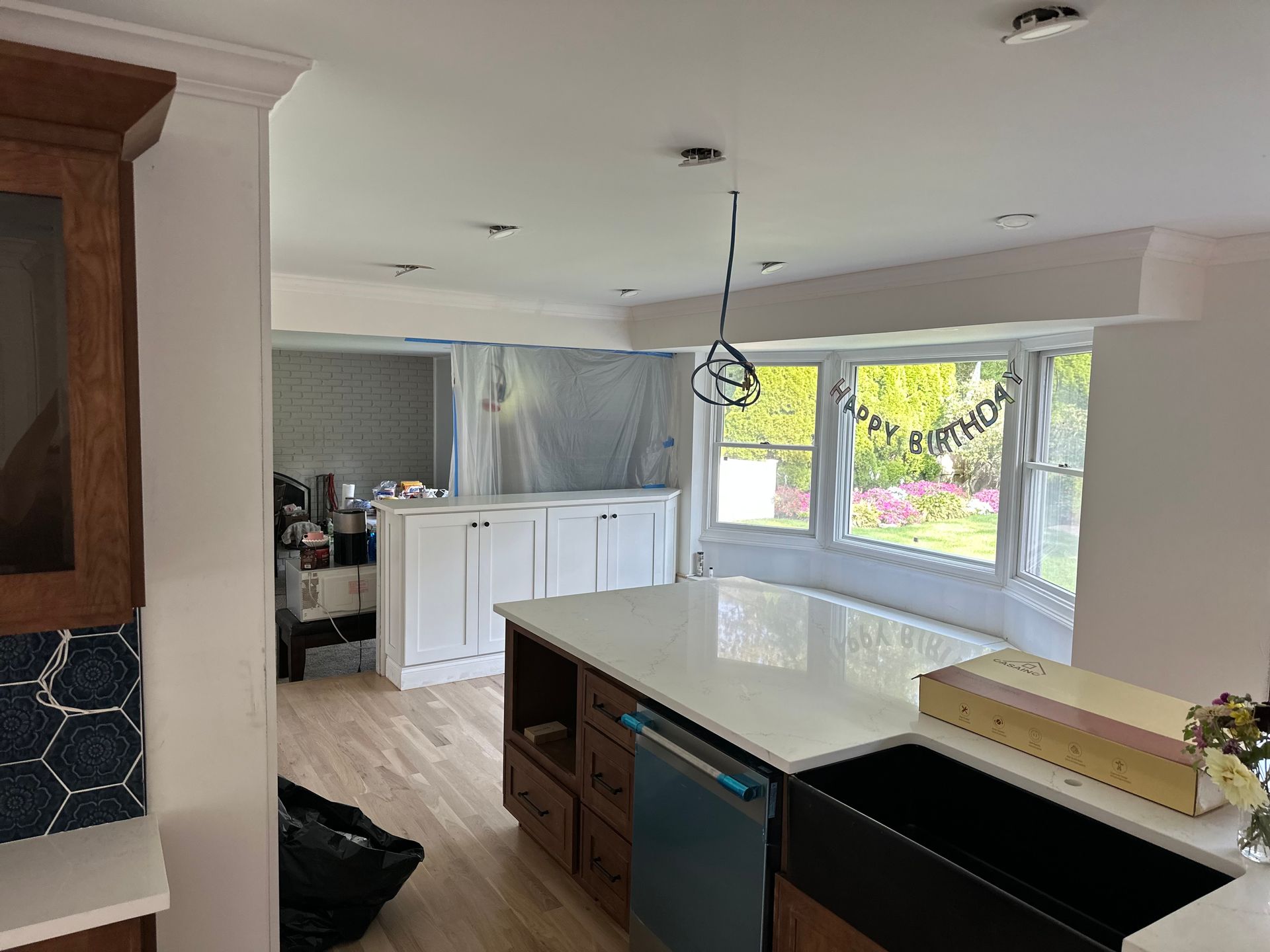Kitchen renovation with new island, cabinets, bay window, and sink; construction debris visible.