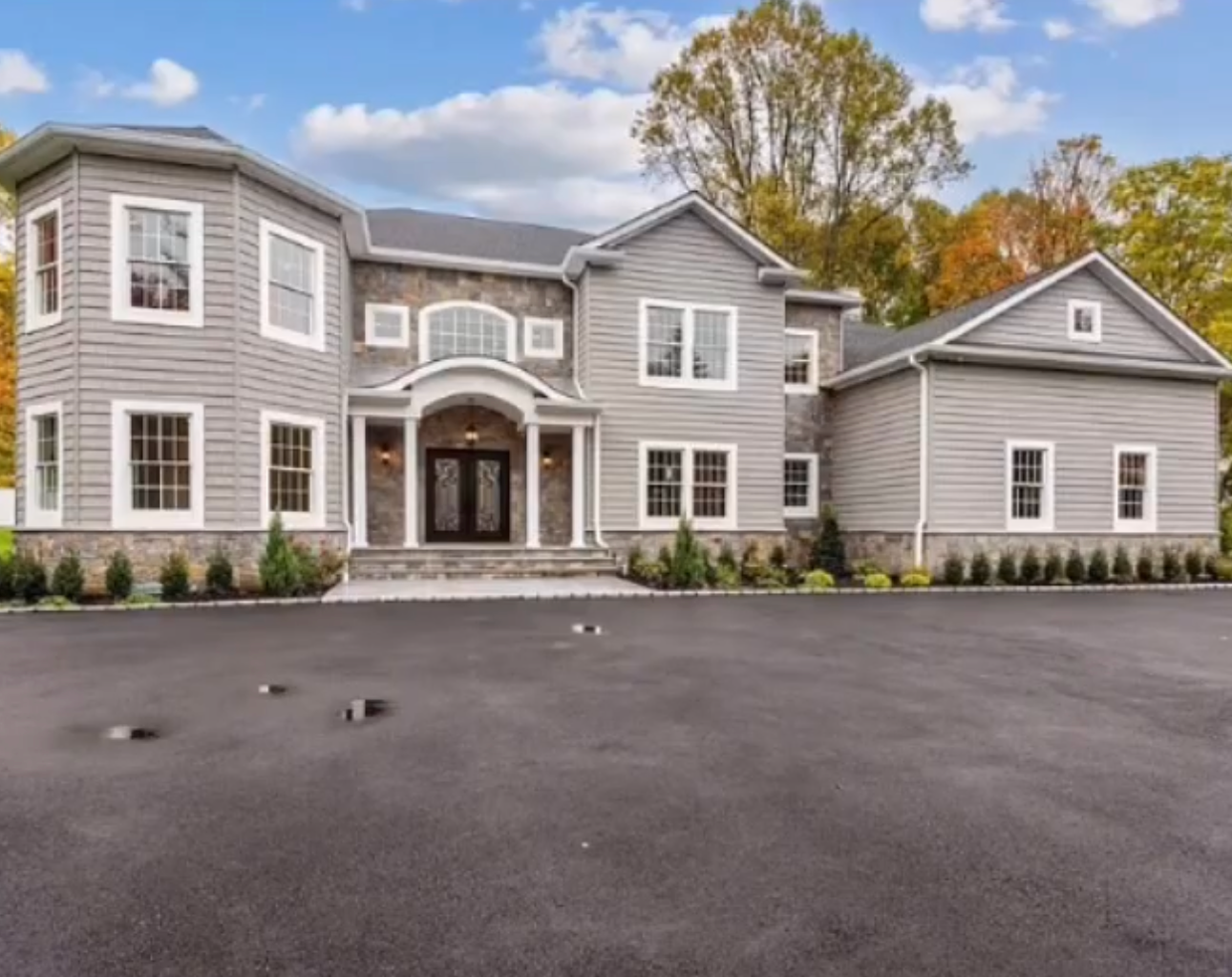 Gray two-story house with stone accents, double front doors, and a large paved driveway.