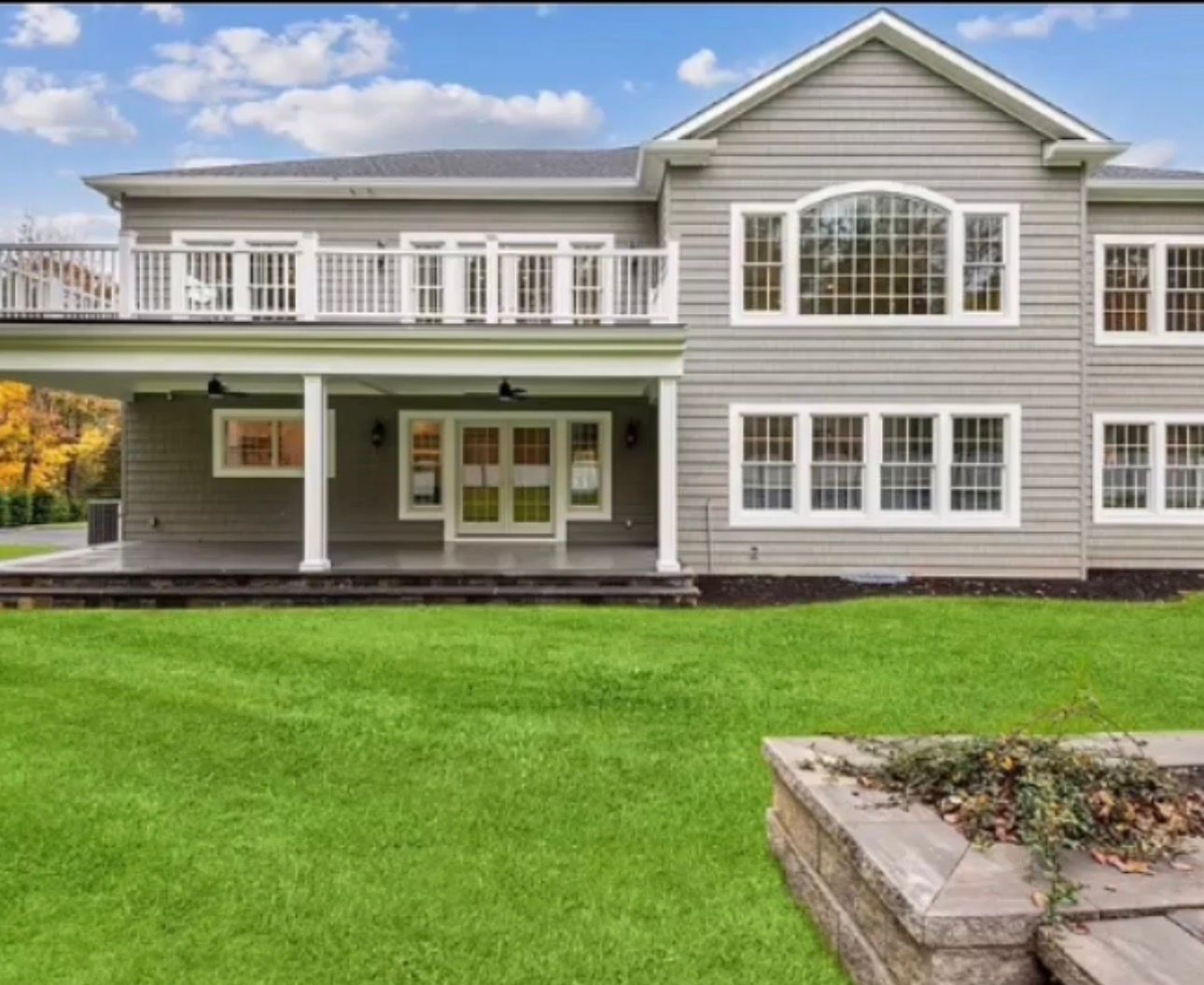 Large gray house with white trim, a second-floor balcony, and a green lawn.