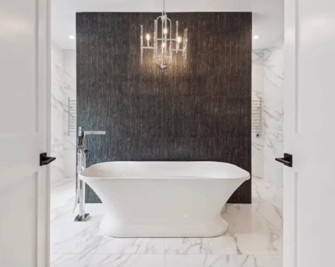 Bathroom with white tub in front of dark textured wall, chandelier overhead.