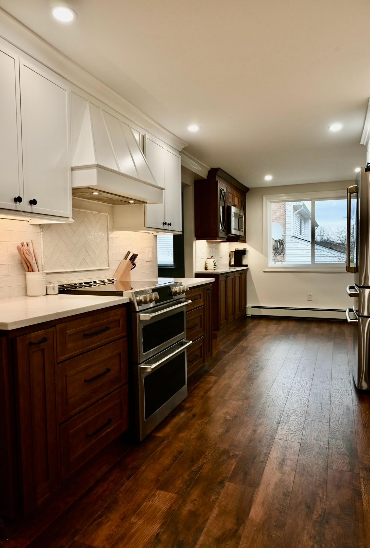 Modern kitchen with two-tone cabinetry, stainless steel appliances, and wood flooring.