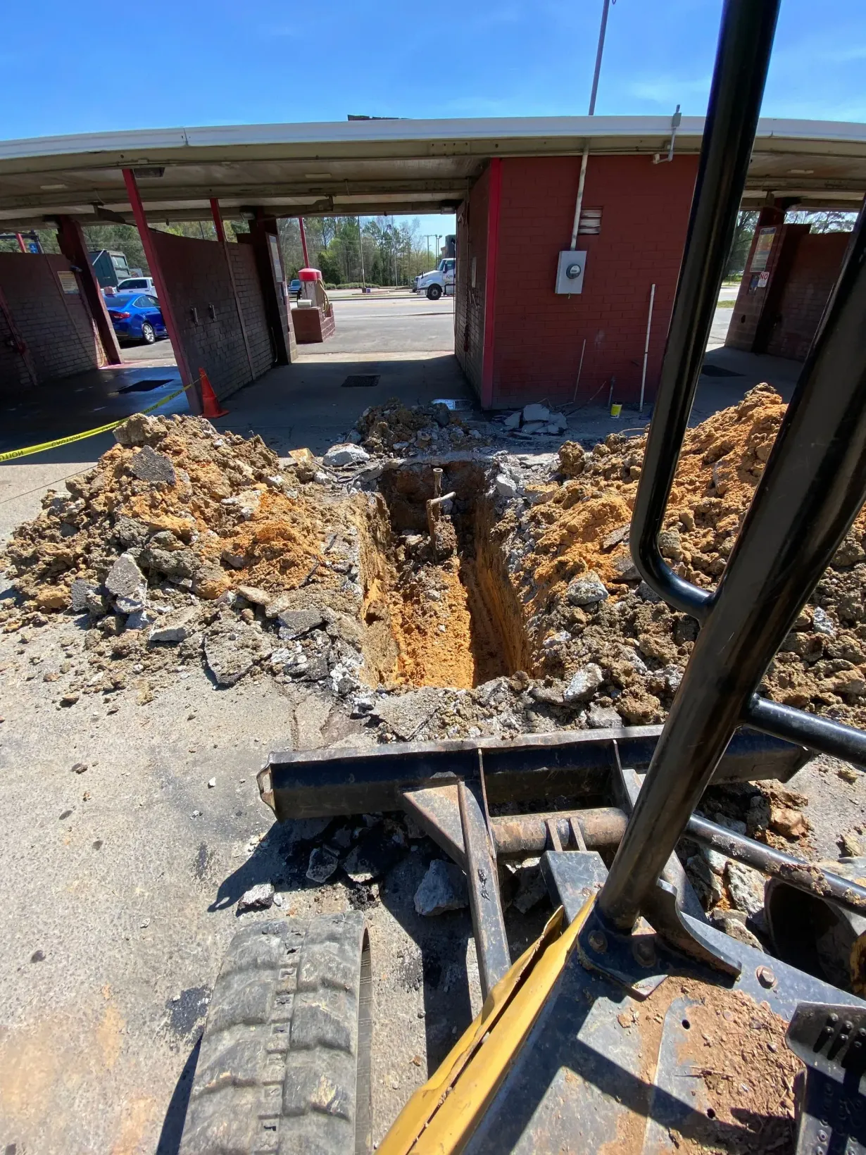 Trench cut in a concrete driveway beside a red building, with debris scattered around