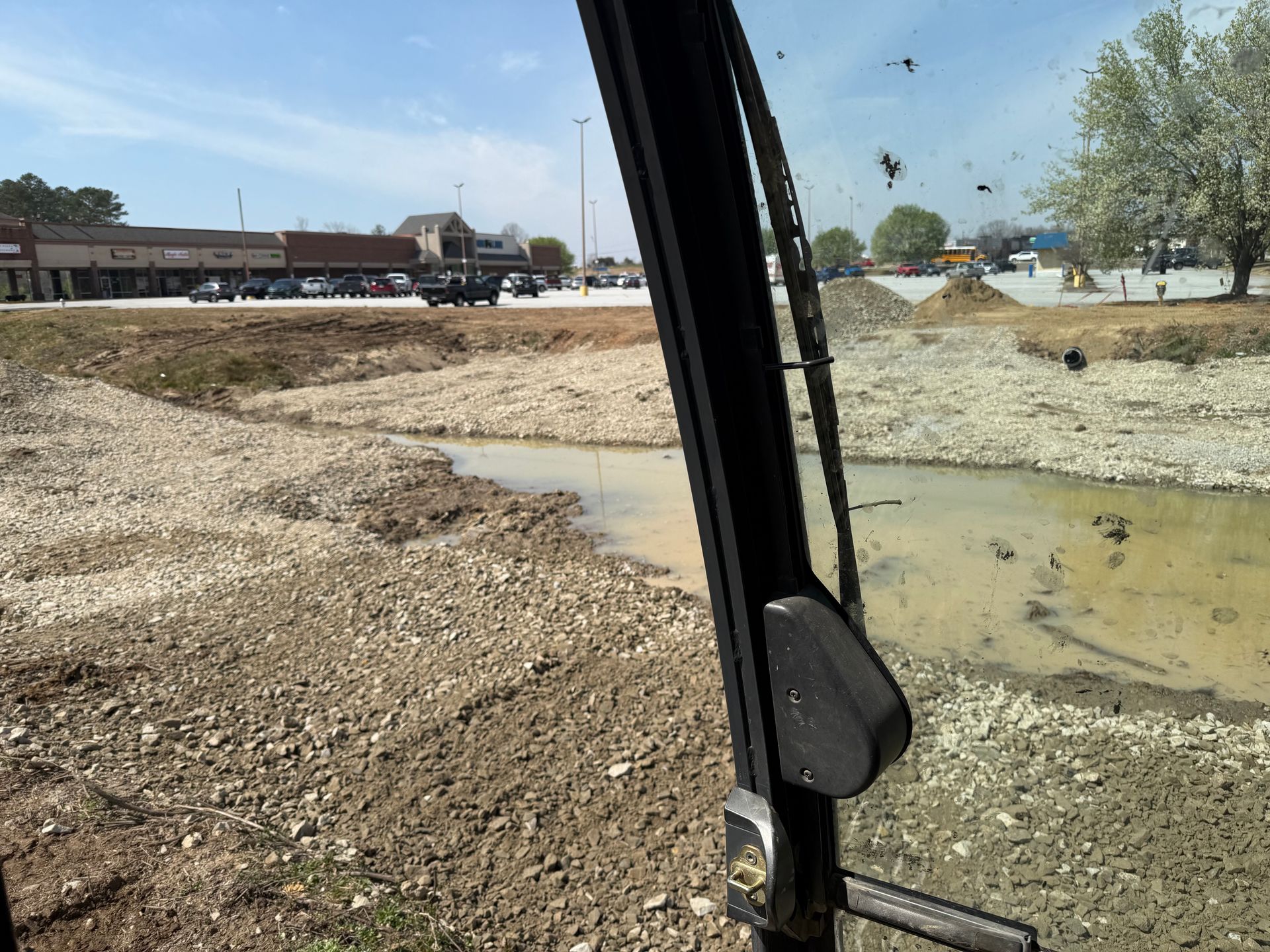 Construction site with a muddy water channel beside a dirt road, viewed from inside a vehicle.