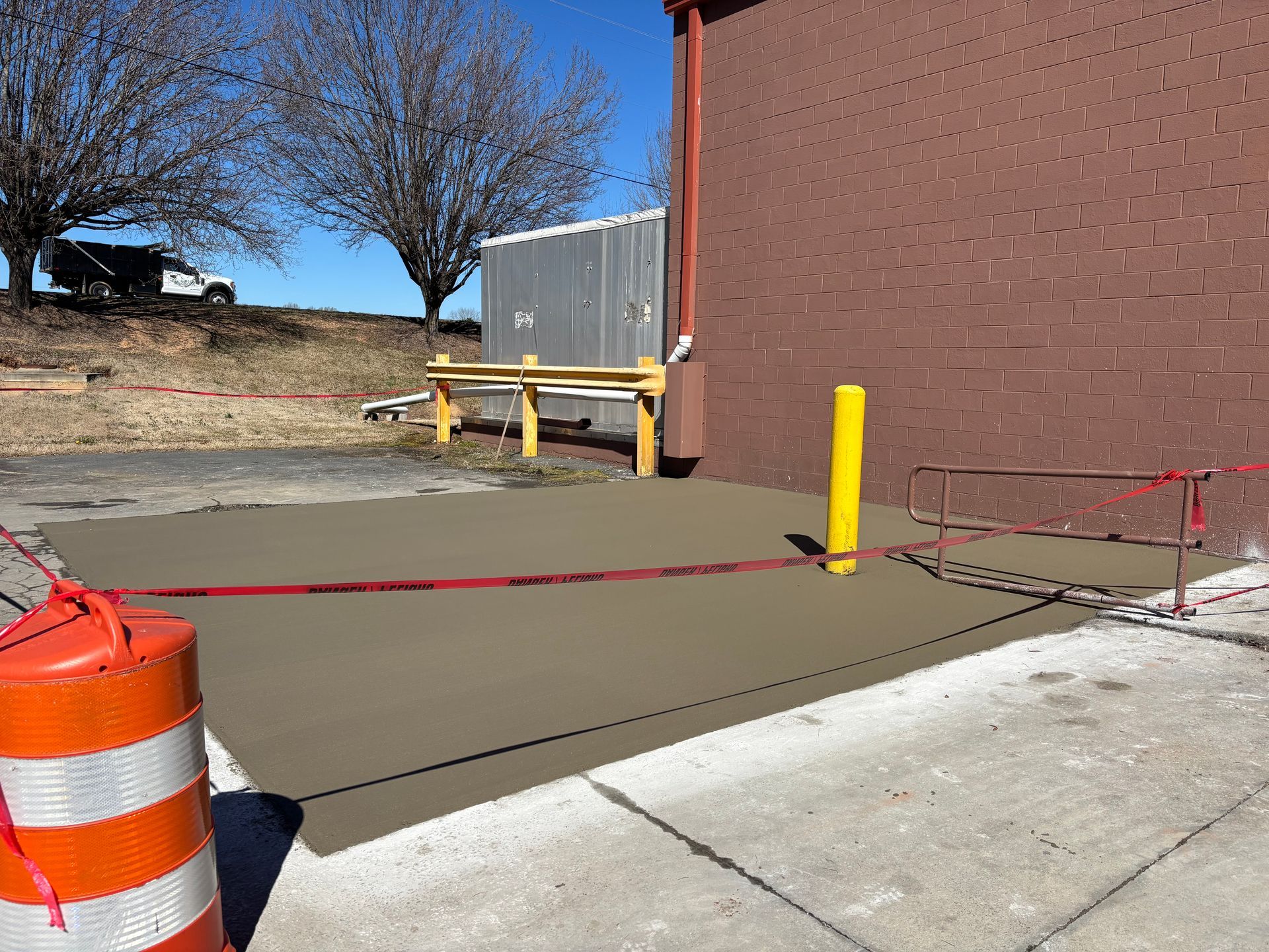 Sidewalk blocked by red caution tape near a brick building and orange traffic barrel.