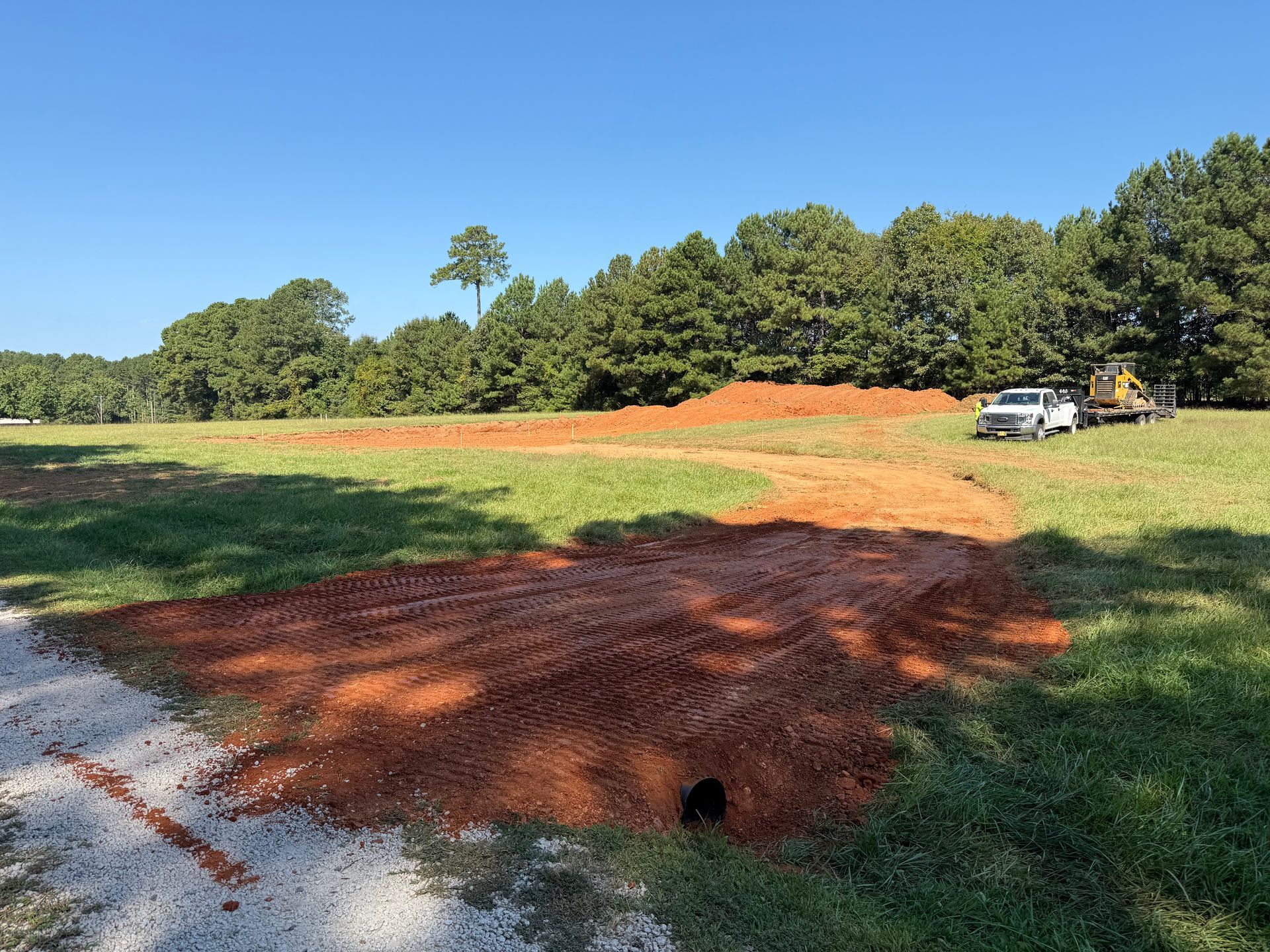 Cleared grassy field with orange dirt mounds, trees in background, and a white truck at right