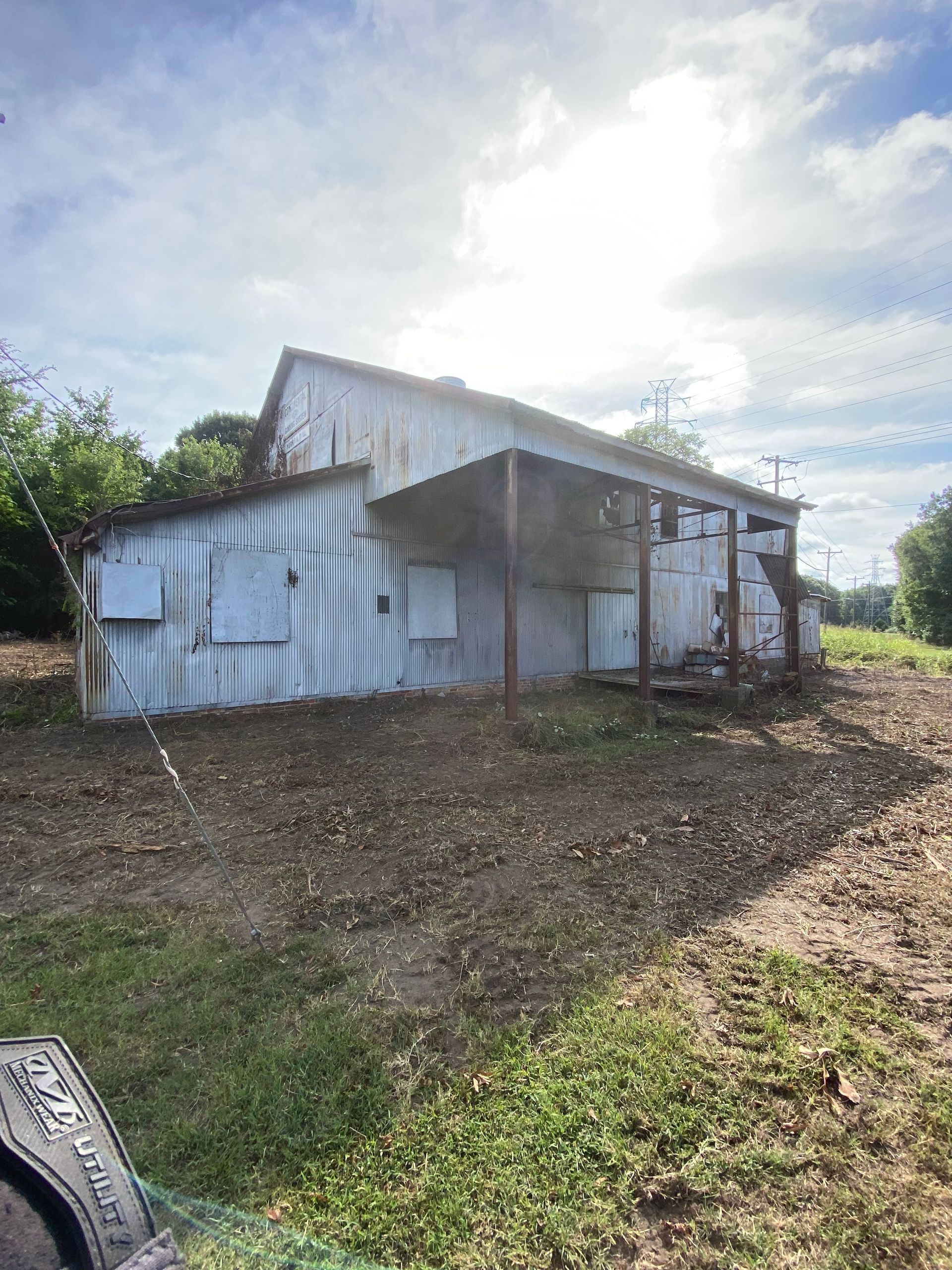 Small white corrugated metal shed with a porch, set on a dirt lot under a cloudy sky.