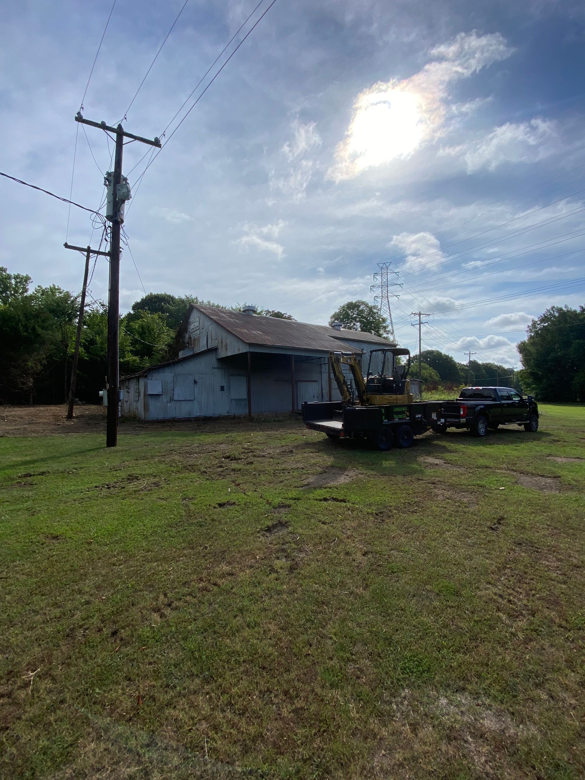 Rural house by a grassy field with a utility pole, parked truck, and bright cloudy sky