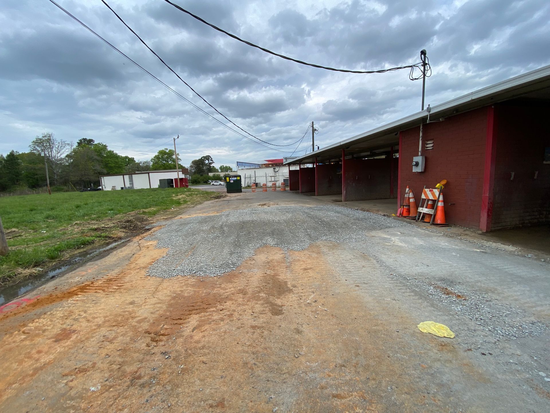 Gravel lot beside a red building under cloudy skies, with utility poles and orange cones nearby