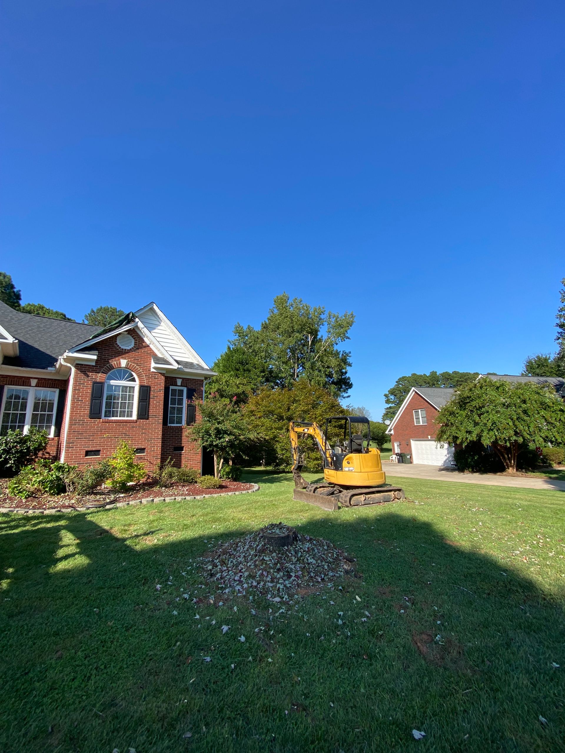 Brick house and garden with green lawn, yellow wheelbarrow, and blue sky