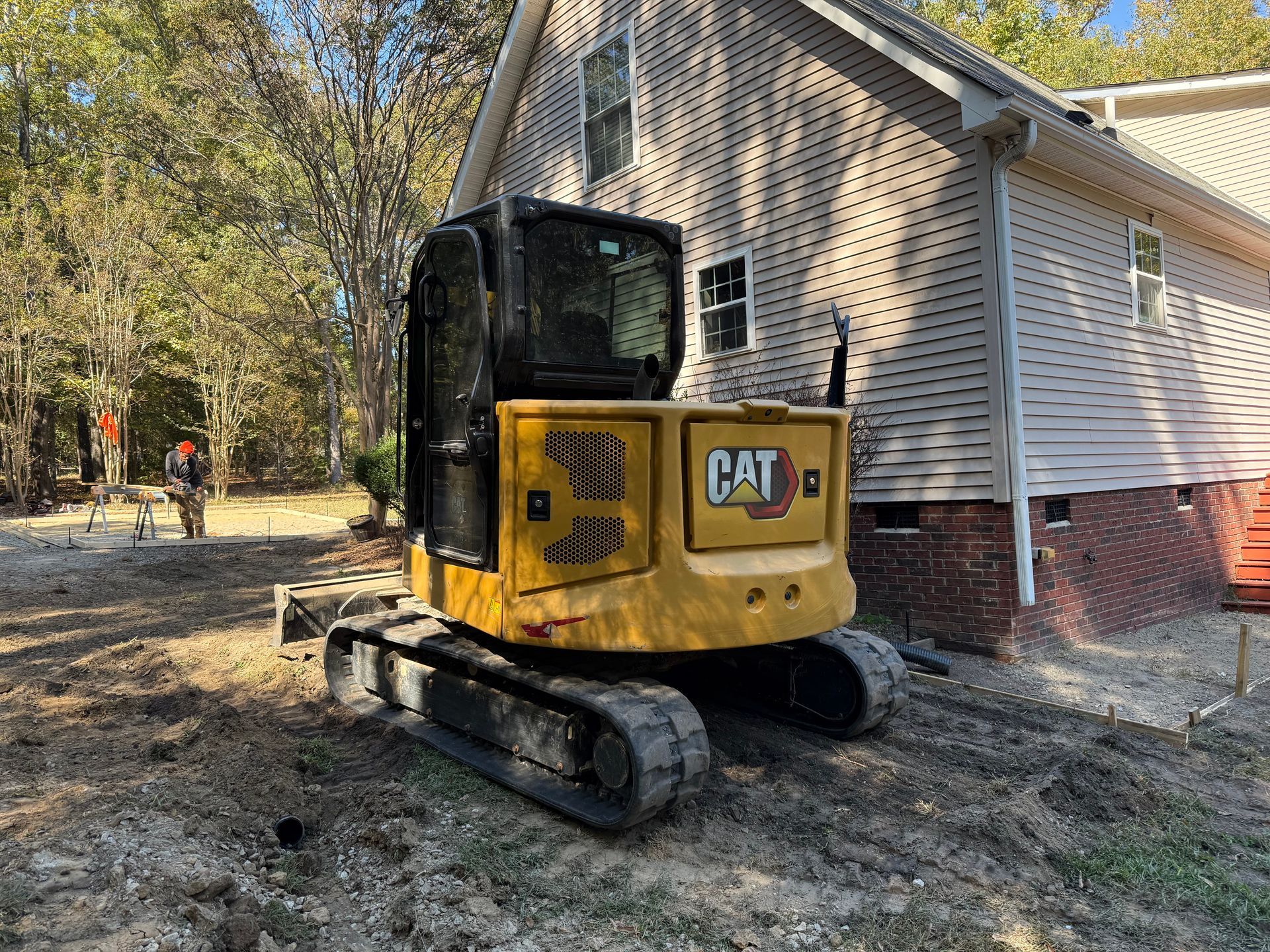 Yellow CAT mini excavator beside a house, working in a wooded yard.