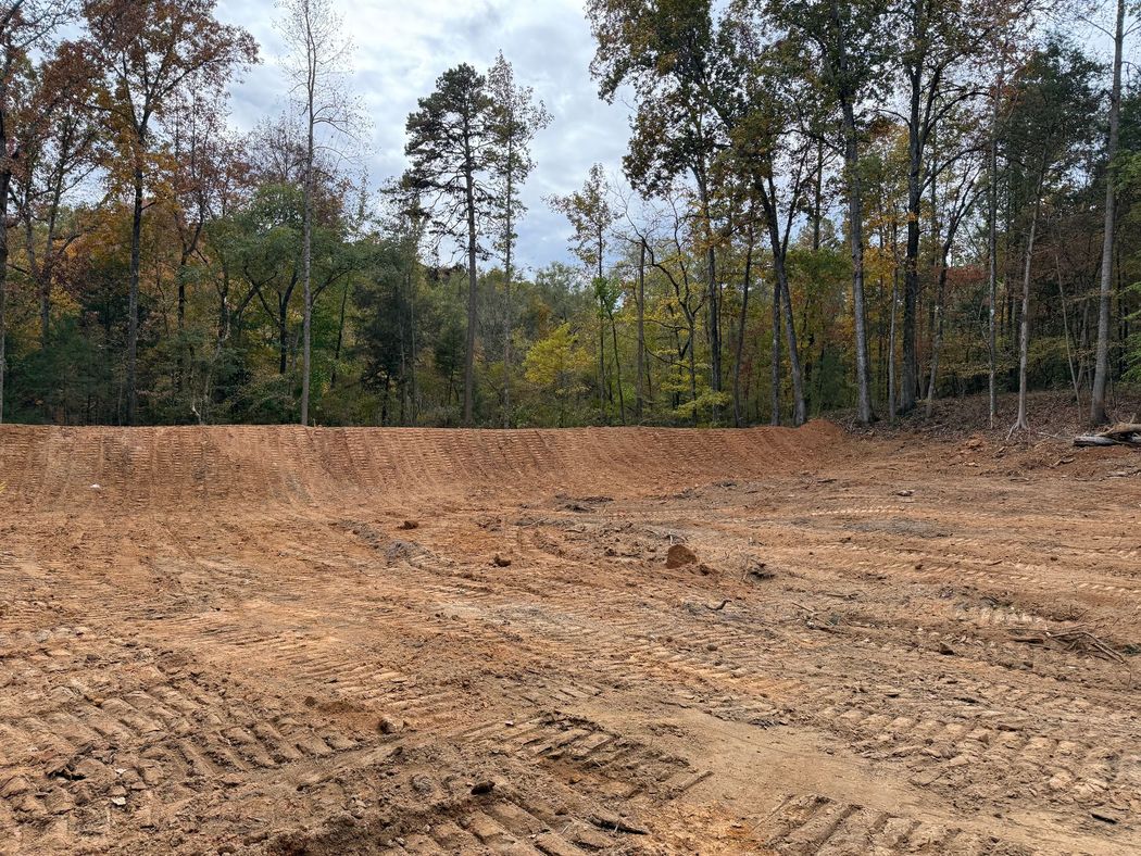 Cleared dirt lot bordered by autumn trees under a cloudy sky