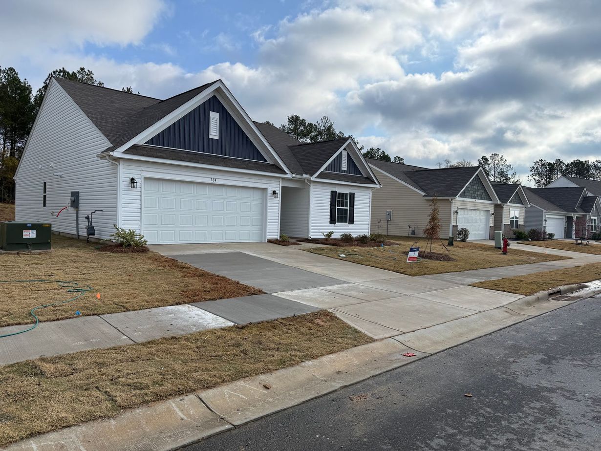Suburban row of gray houses with white garages, sloped driveways, and cloudy sky along a quiet street
