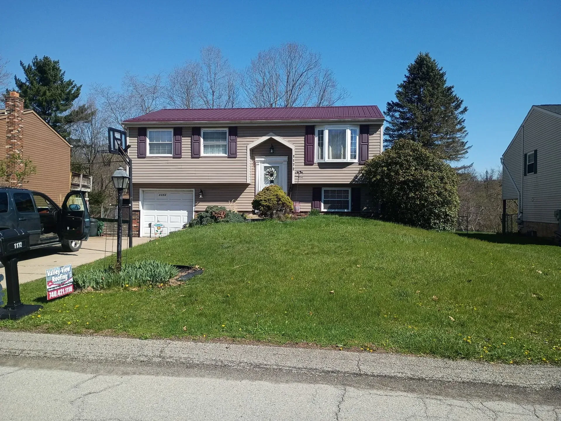 Suburban two-story house with a red roof, front lawn, driveway, and garage on a sunny day