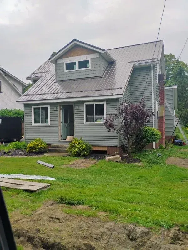 Gray two-story house with dormer, white trim, and a wet lawn in the foreground