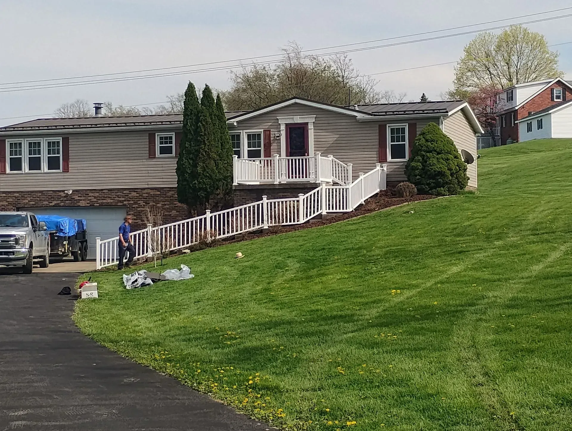 Suburban house with front porch, steep green lawn, and driveway on a cloudy day