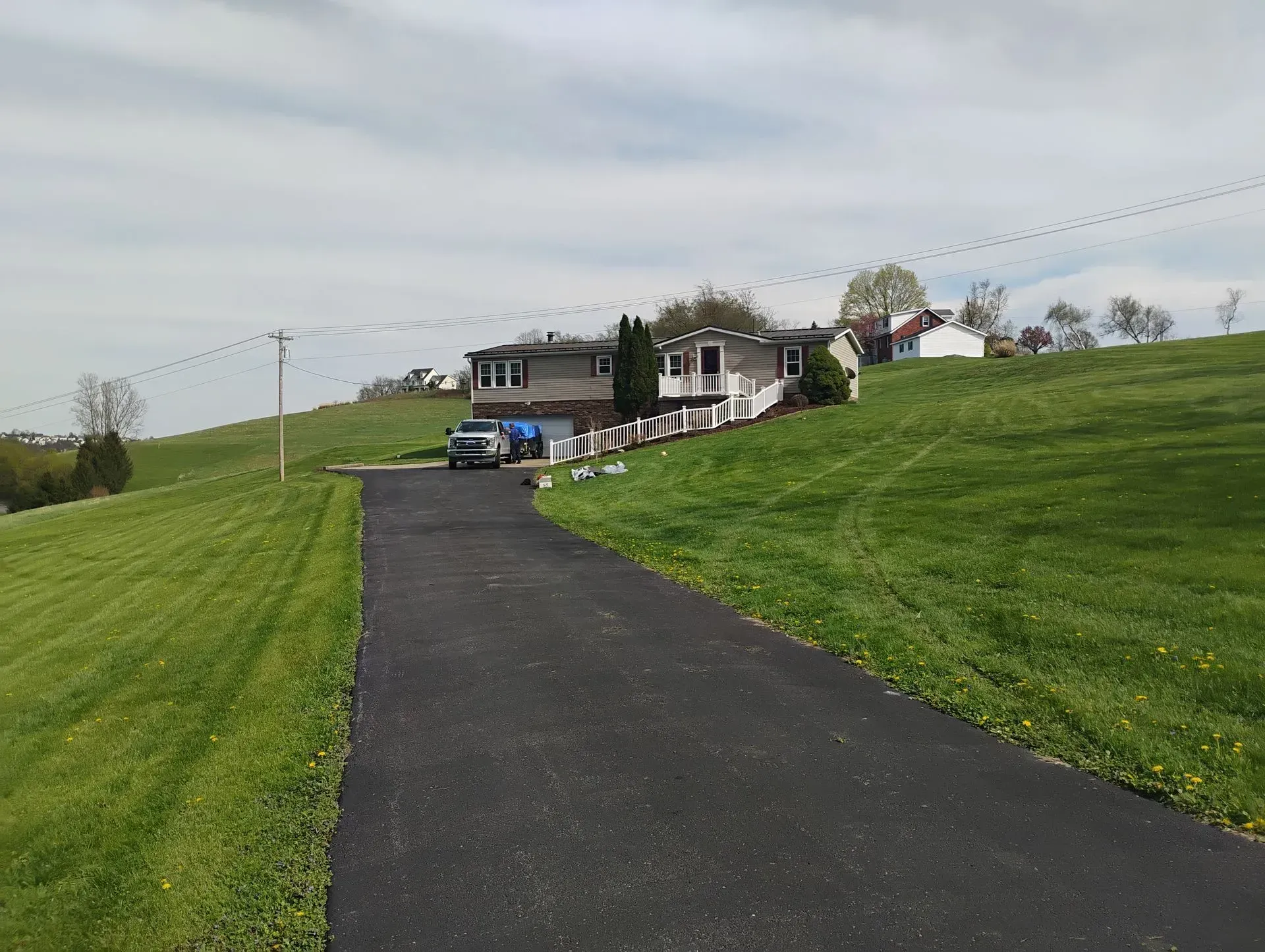 Long driveway leading to a house on a grassy hill under a cloudy sky