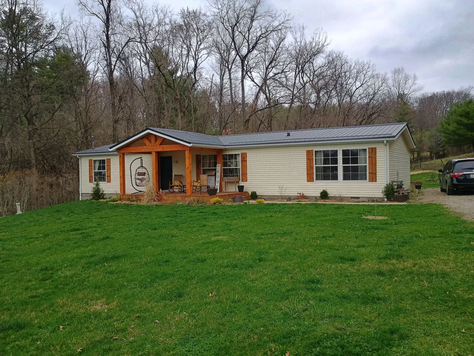 Single-story cream house with orange porch in a grassy yard, backed by leafless trees under cloudy sky