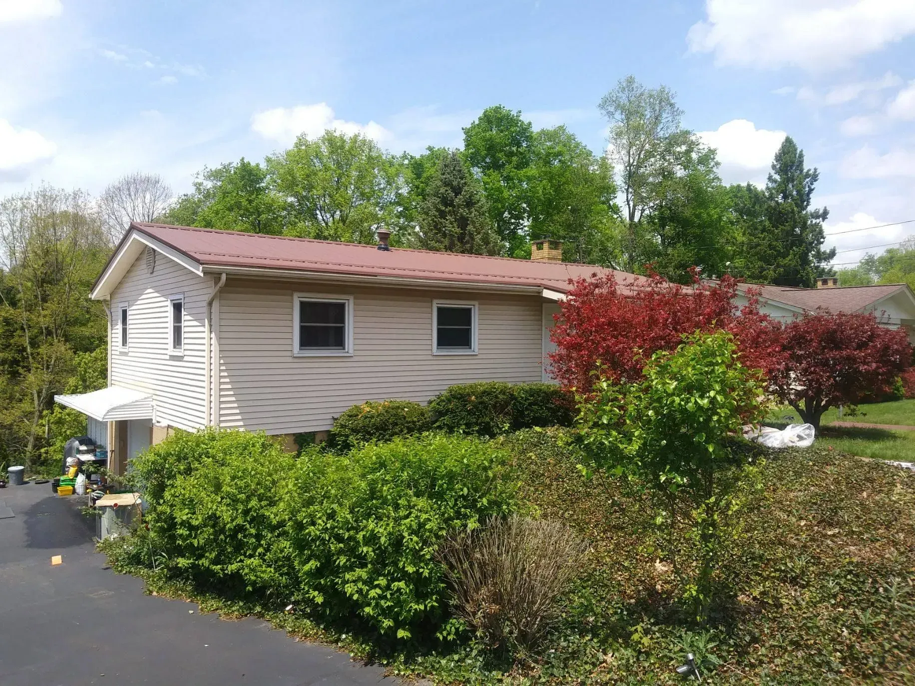 Suburban house with beige siding, red roof, and landscaped shrubs beside a paved driveway