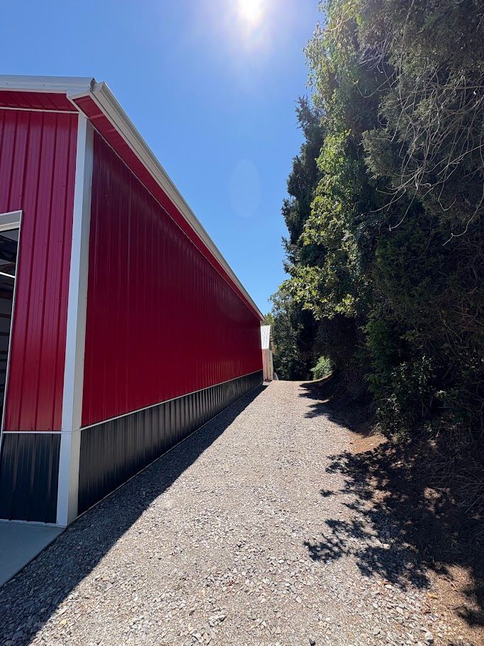 Red barn with gravel path, trees, and bright sun.