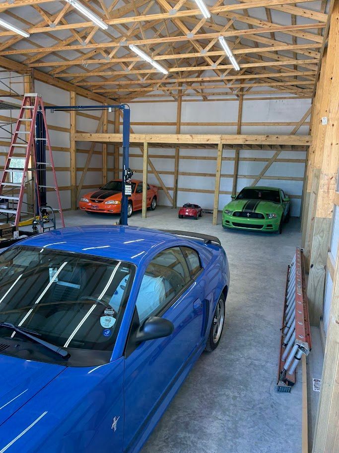 Blue car parked in a garage with three Mustangs; one orange, one red, and one green.