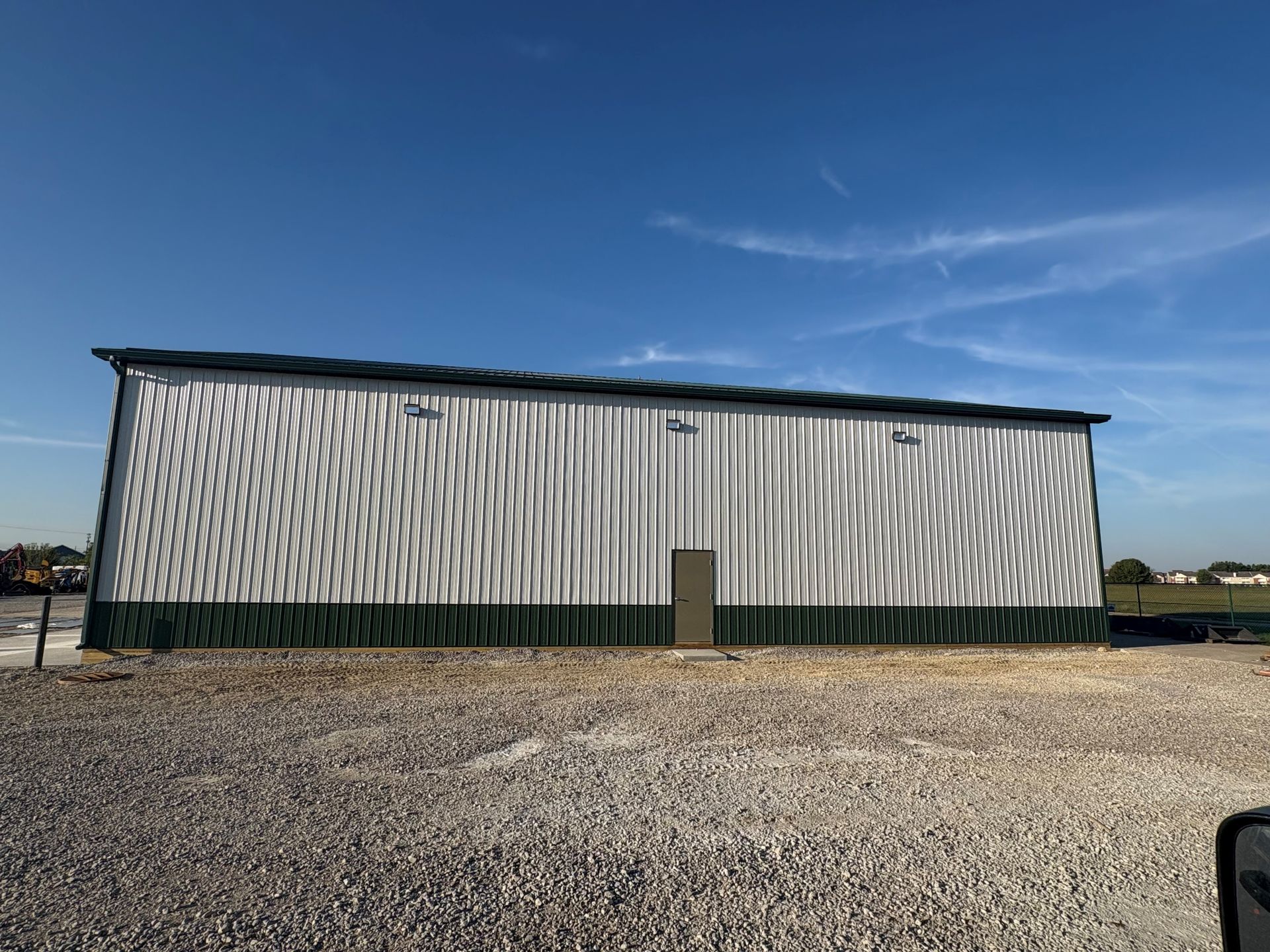 Metal warehouse building with green trim, against a blue sky.