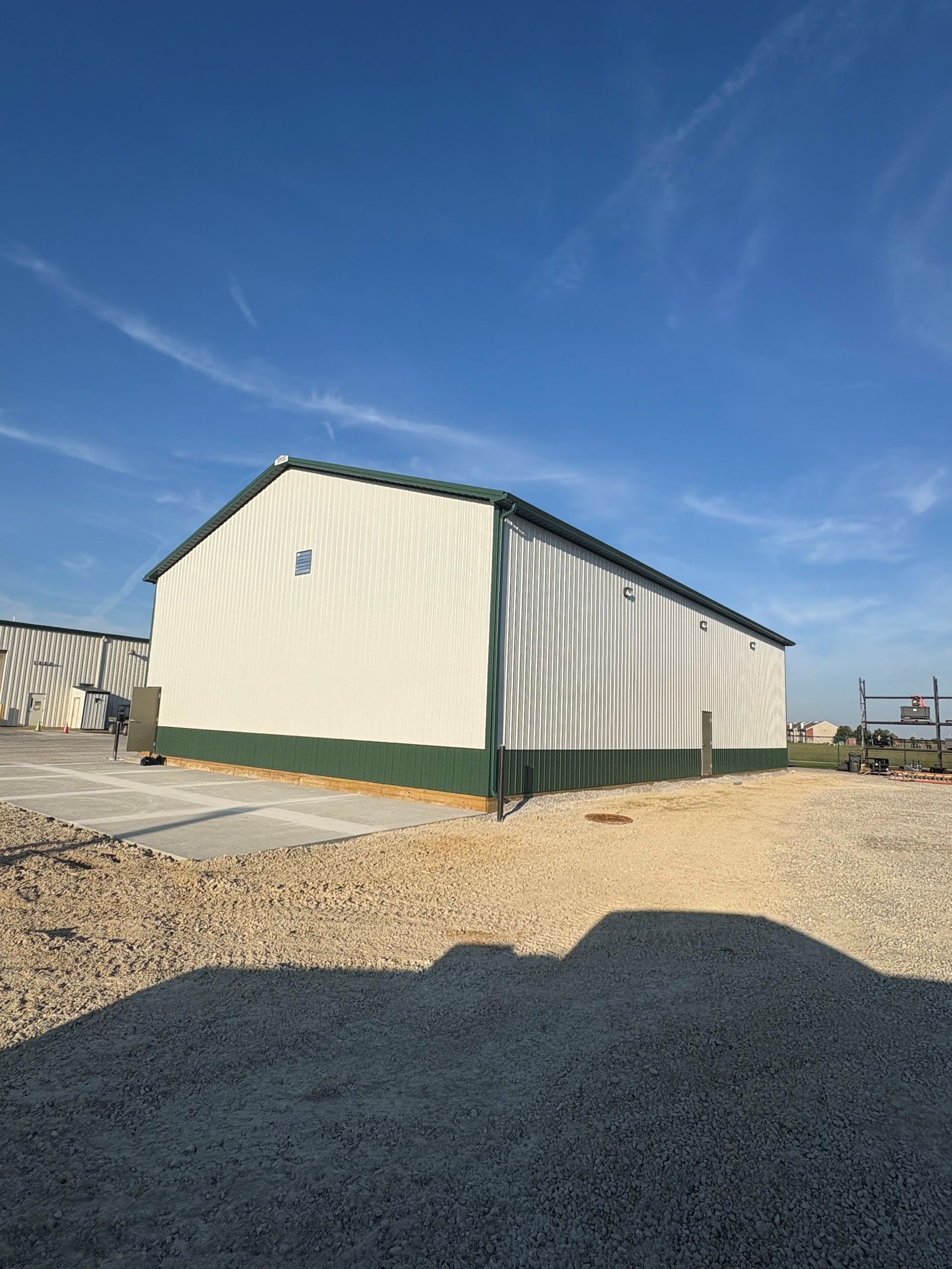 White and green metal building on a gravel lot under a blue sky.