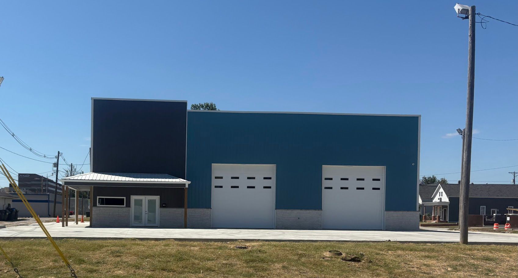 Building with blue and dark blue walls, white garage doors, and a small entrance under a canopy, against a blue sky.