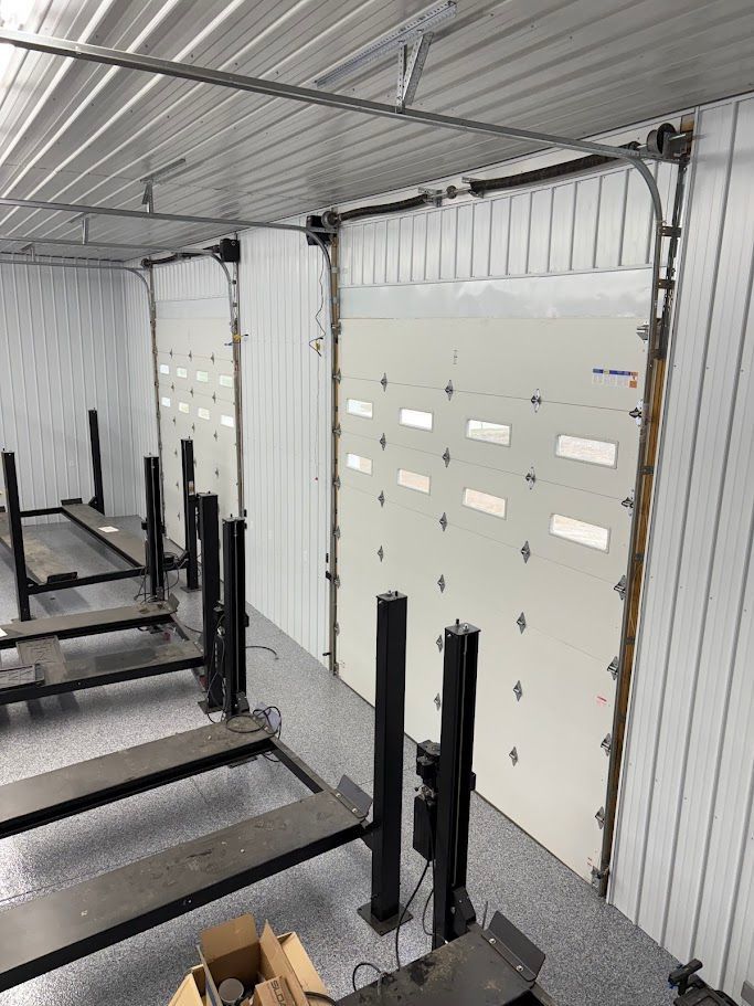 Garage interior with two large white garage doors, car lifts, and metal siding.