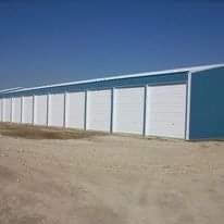 Blue and white storage units with roll-up doors, set against a clear blue sky and a dirt lot.