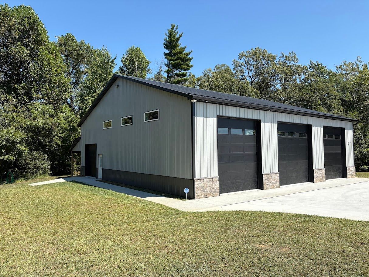 Gray metal building with three garage doors and dark trim, in a grassy setting.
