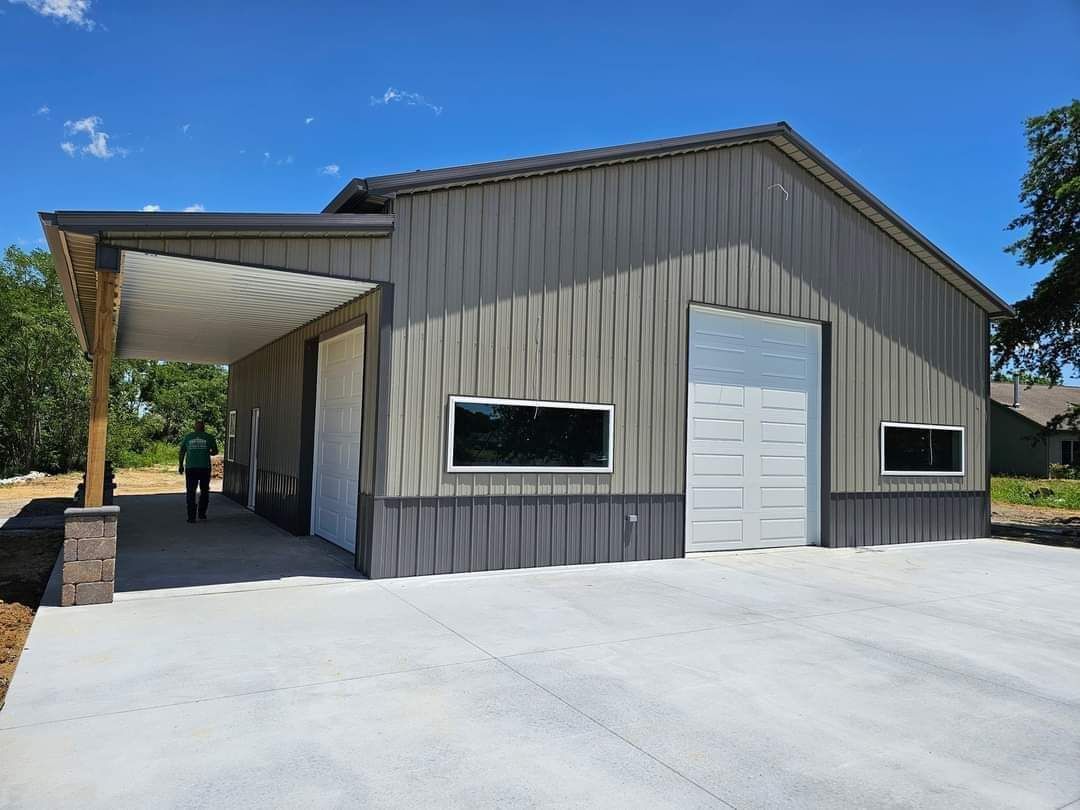 Gray metal building with a white garage door, carport, and concrete driveway.