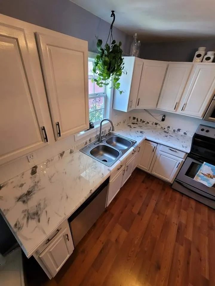 White kitchen with marble countertops, stainless steel sink, and cabinets; hardwood floors.