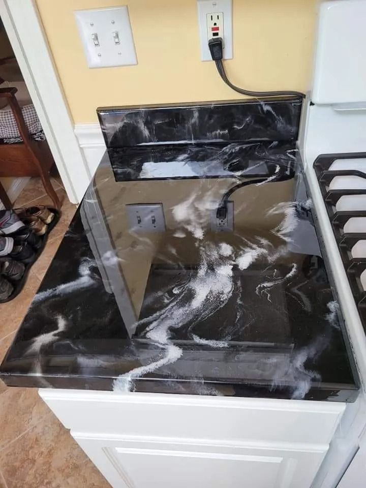 Black and white marbled countertop with outlets and electrical cord next to a white stove.