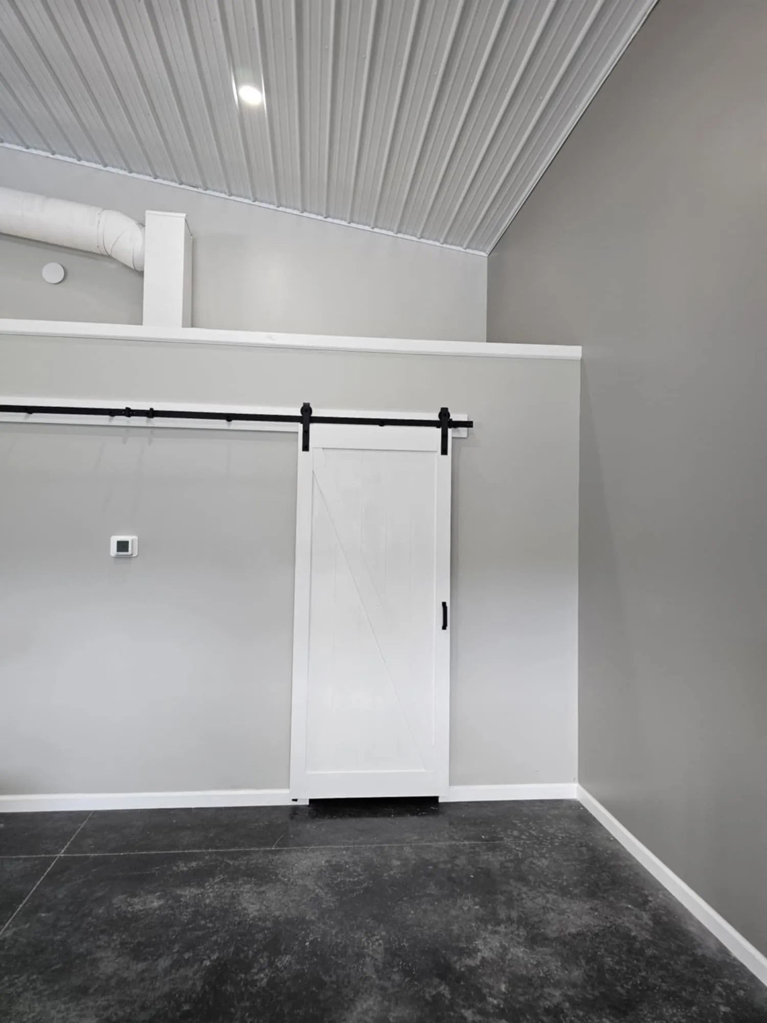 Gray room with white sliding barn door; concrete floor, metal ceiling.