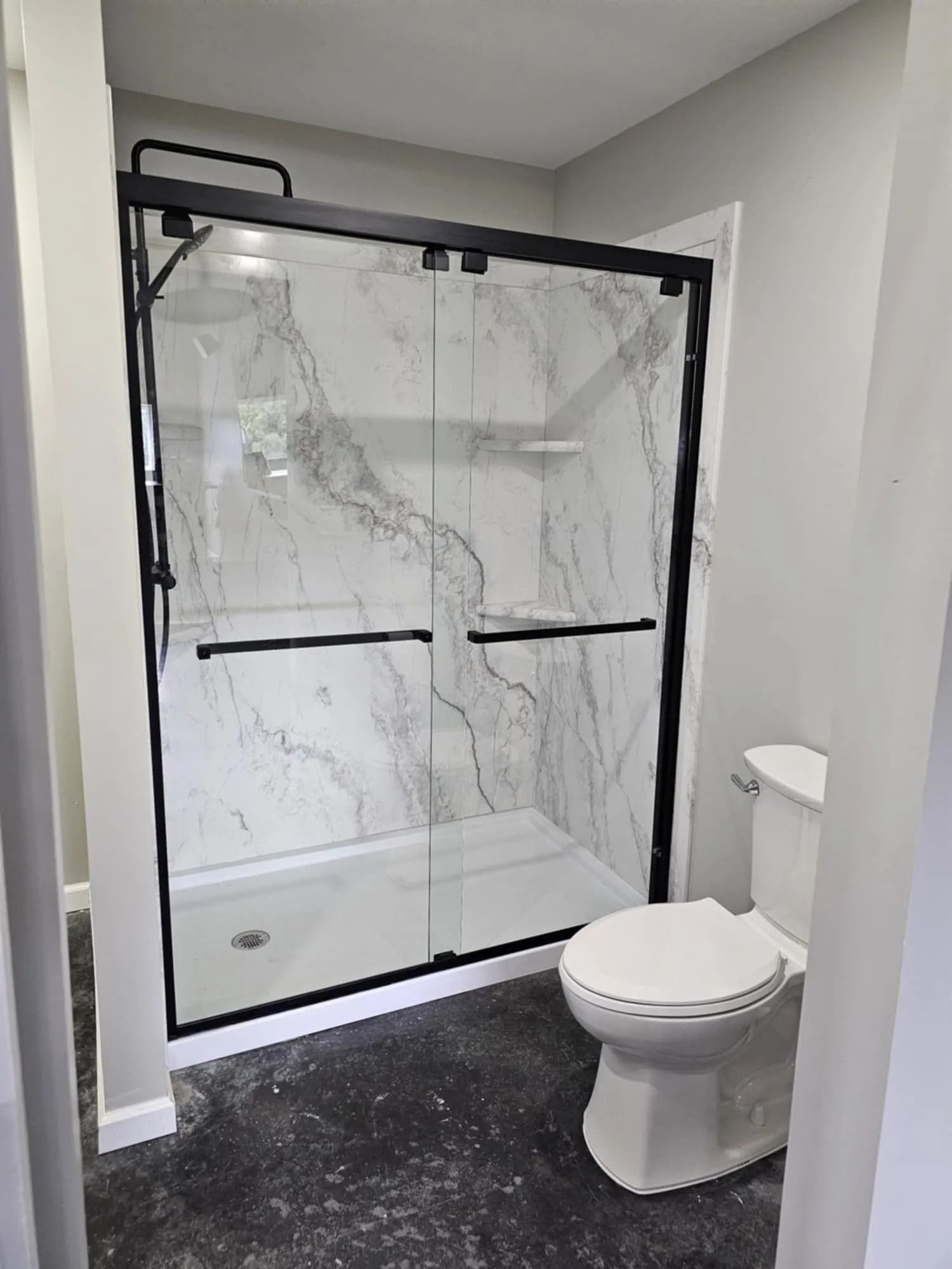 Bathroom with white marble shower, black framed glass doors, and a white toilet.