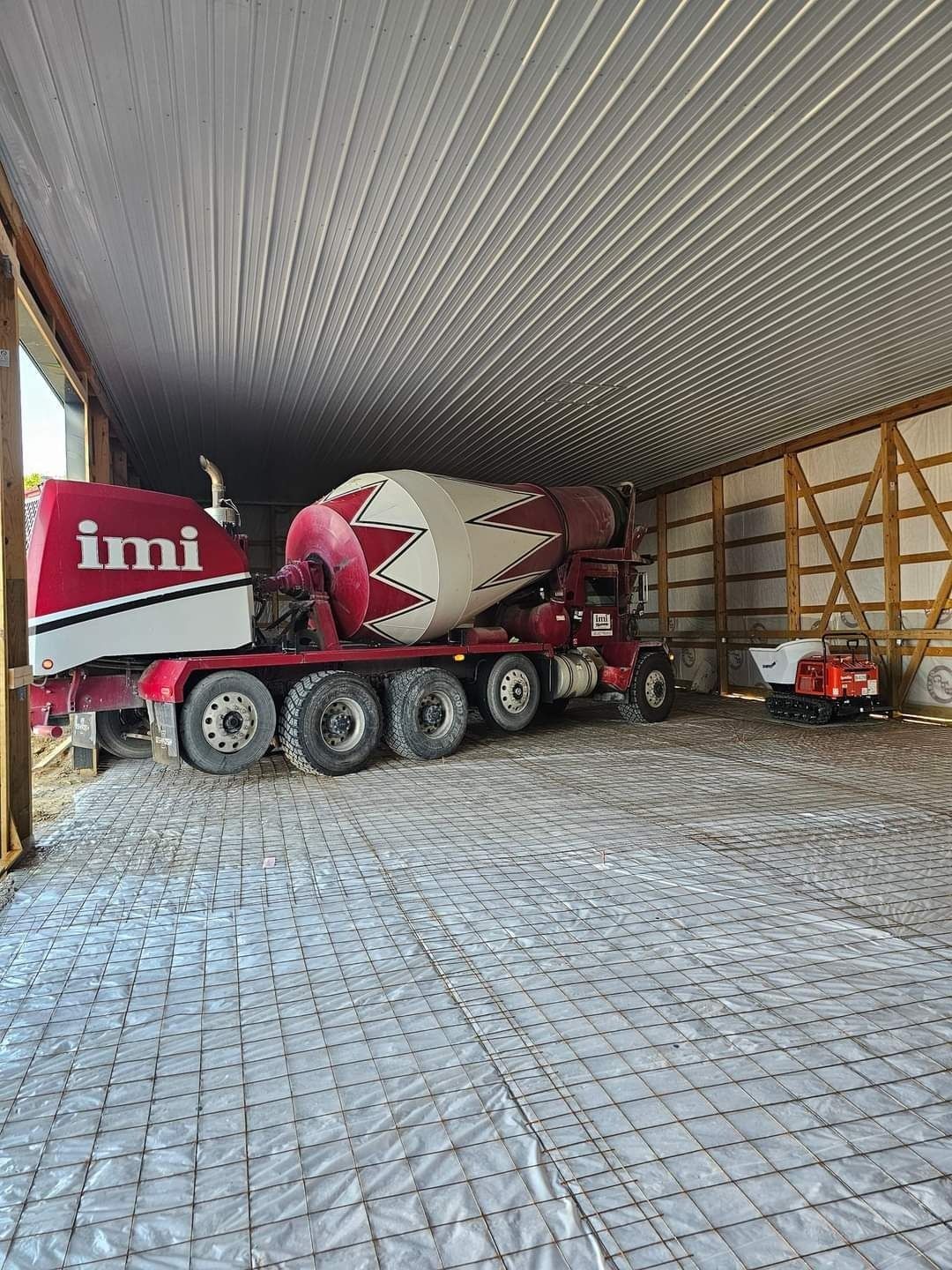 A concrete truck pouring concrete inside a barn with wire mesh on the floor.
