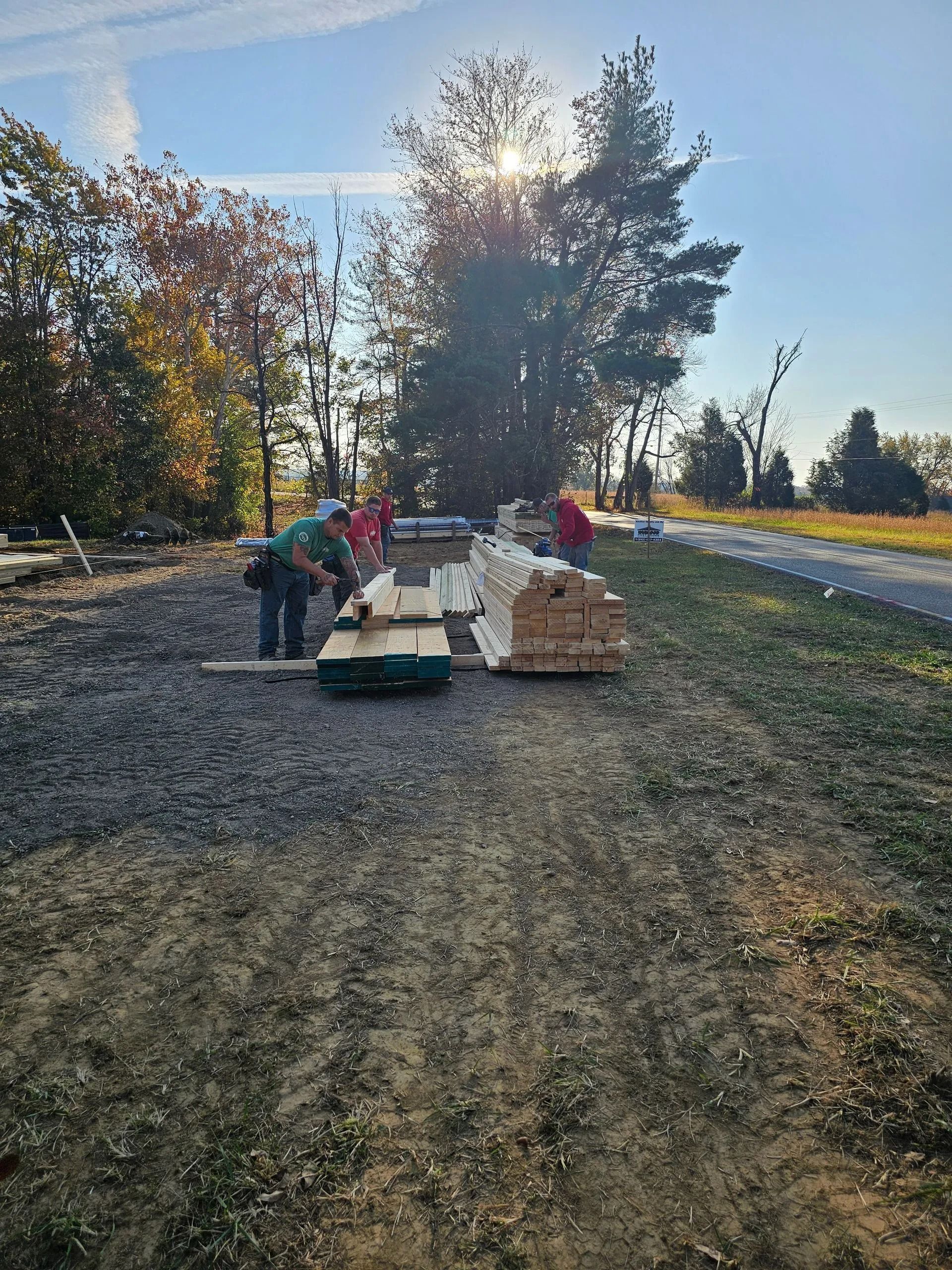 Construction workers sorting lumber outdoors on a gravel area under a bright sun.