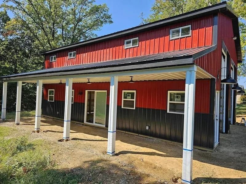 Red and black barn-style building with white pillars supporting a covered porch, windows, and black roof.