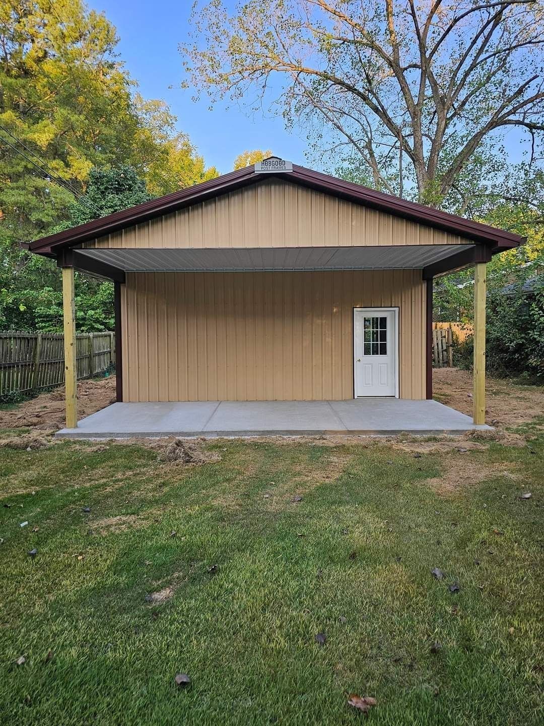 Tan metal building with brown roof and concrete slab, white door, on green grass.