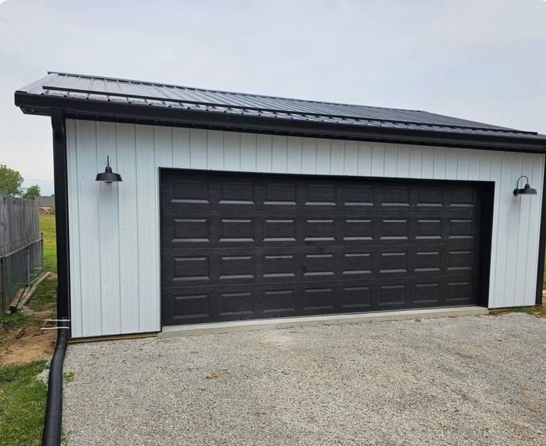 Black garage door on a white building with black trim, gravel driveway.
