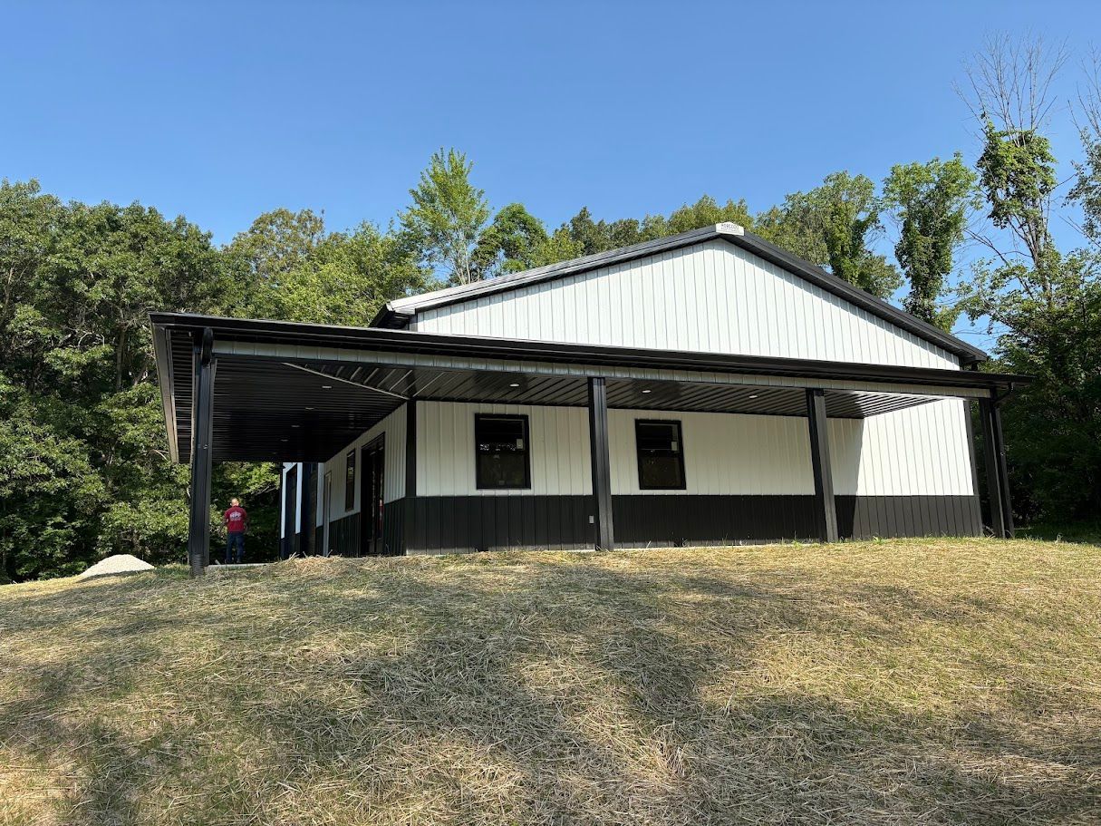 A white and black barn-like building with a covered porch, on a grassy hill, under a blue sky.