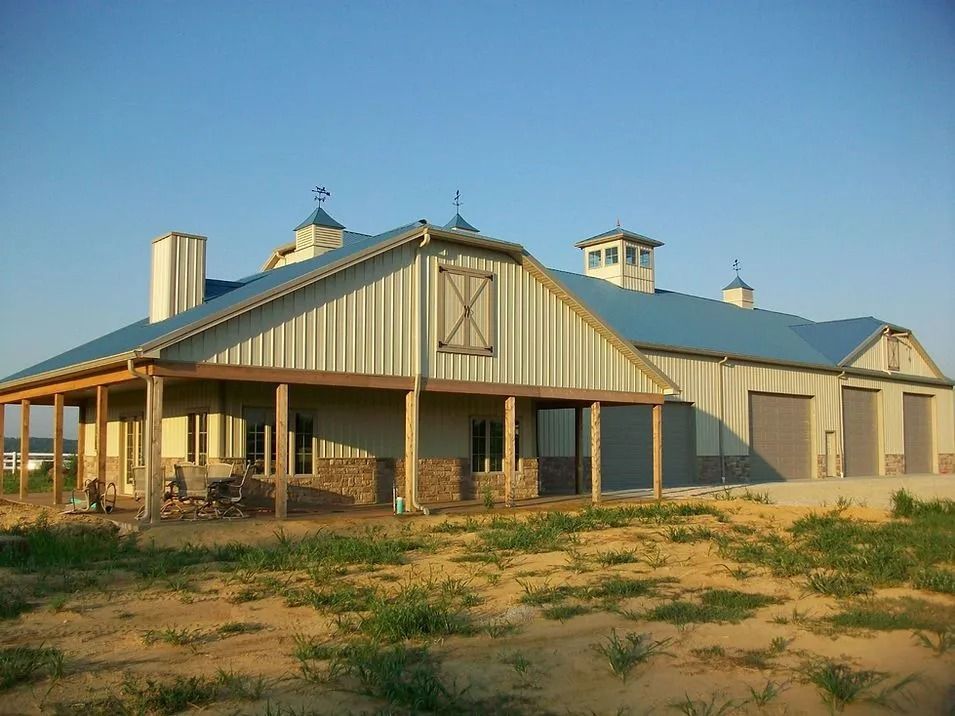 Barn-style building with a blue roof and tan siding, porch, and garage doors against a clear sky.