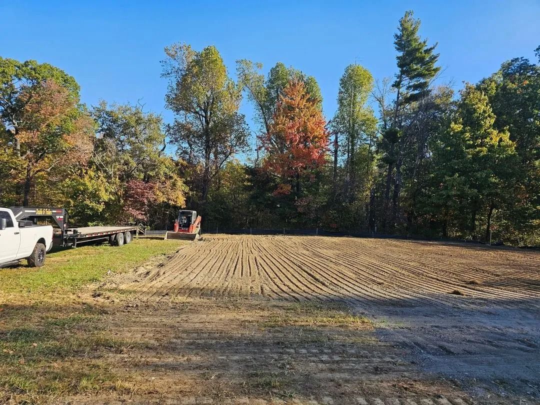 Cleared land with tractor marks; trees in the background; white truck and trailer on left.