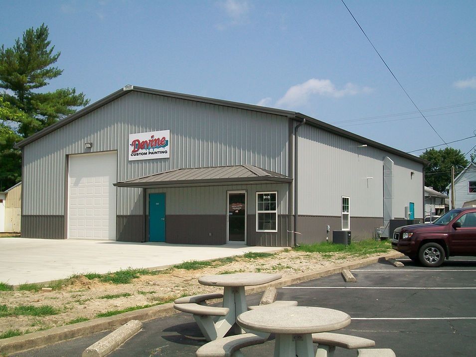 Metal building with a sign, parking lot with picnic tables, and a maroon SUV parked.
