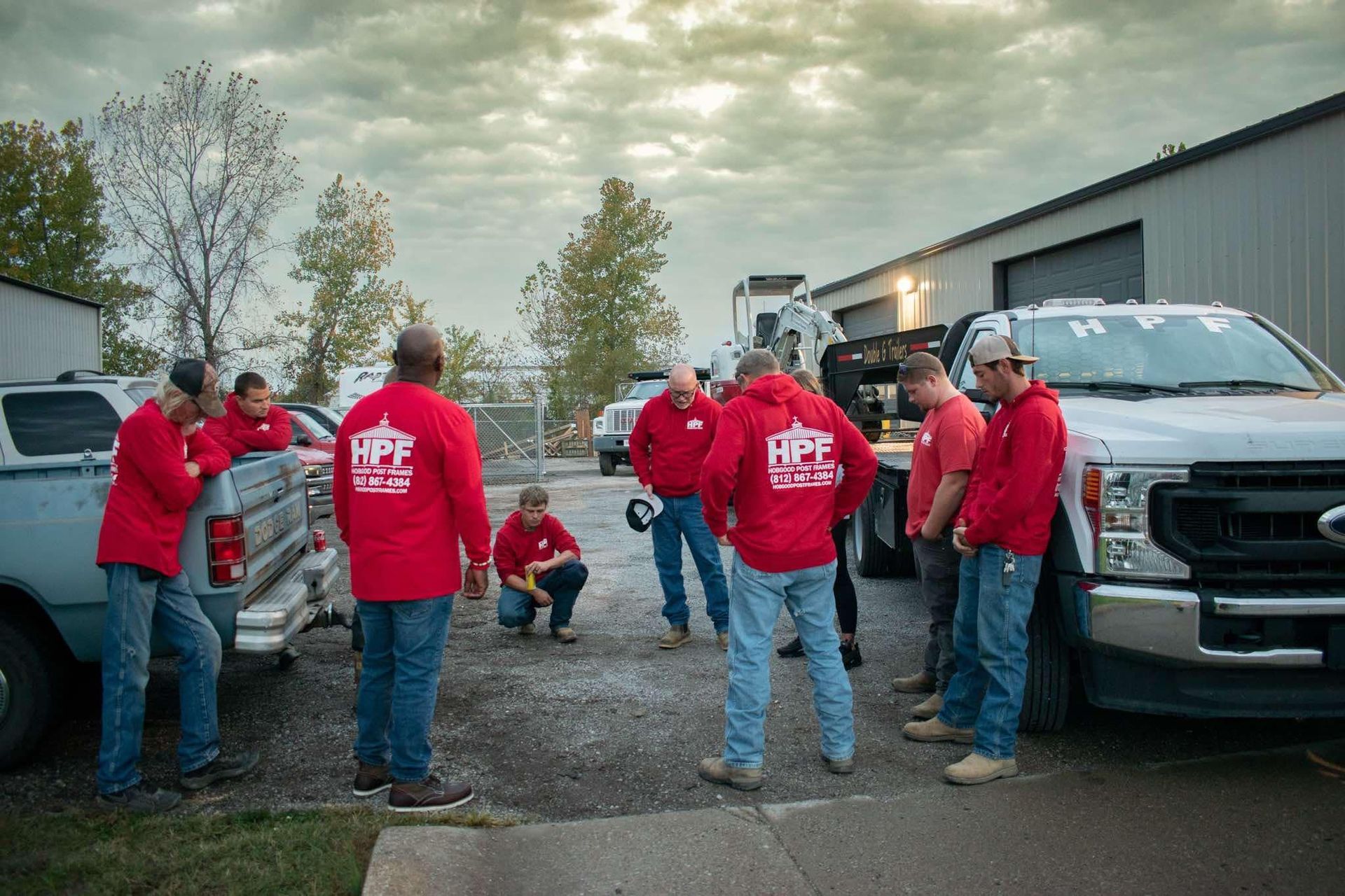 A group in red hoodies gathered beside trucks outside a building at dusk.