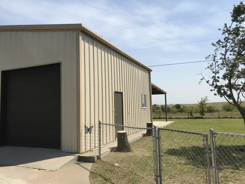 A metal building with a black garage door is surrounded by a chain link fence.