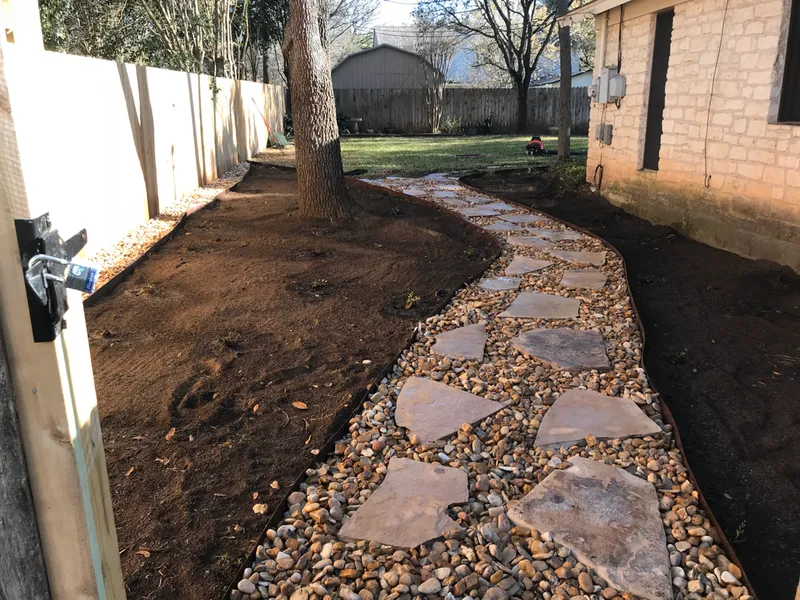 A stone walkway leading to a house in a backyard
