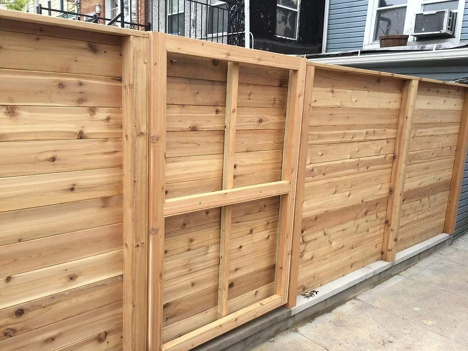 Wooden fence with a gate, in an outdoor setting. The fence and gate are made of horizontal wooden planks.