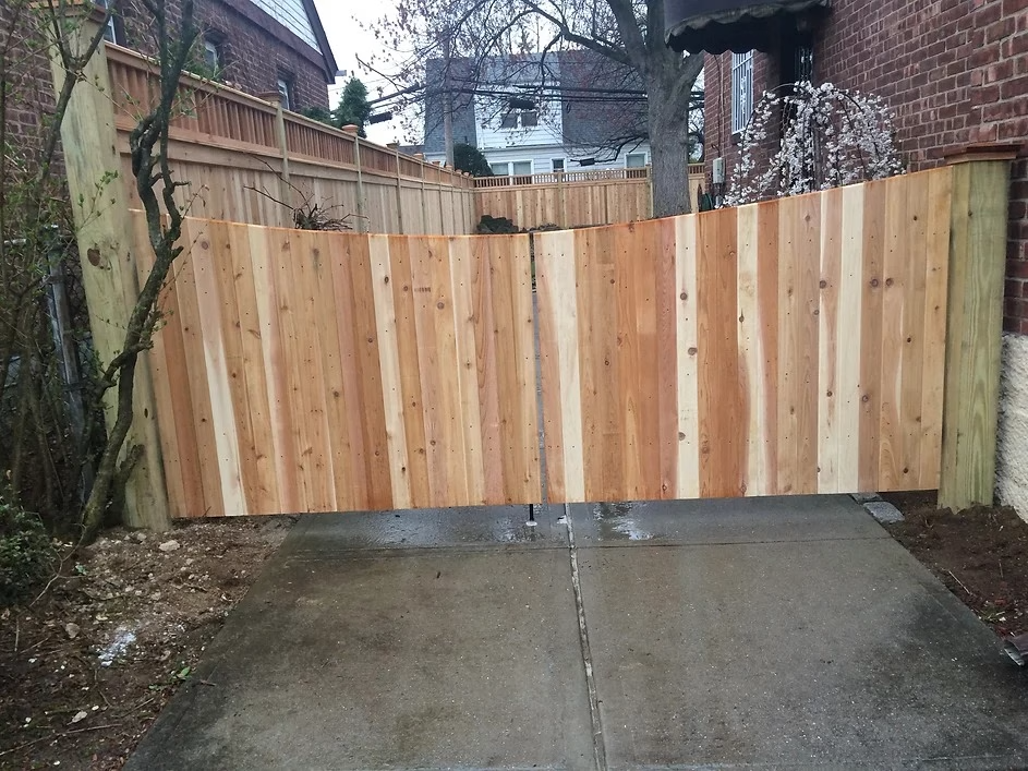 Wooden fence gate, closed, on a concrete driveway. Wooden fence in background.