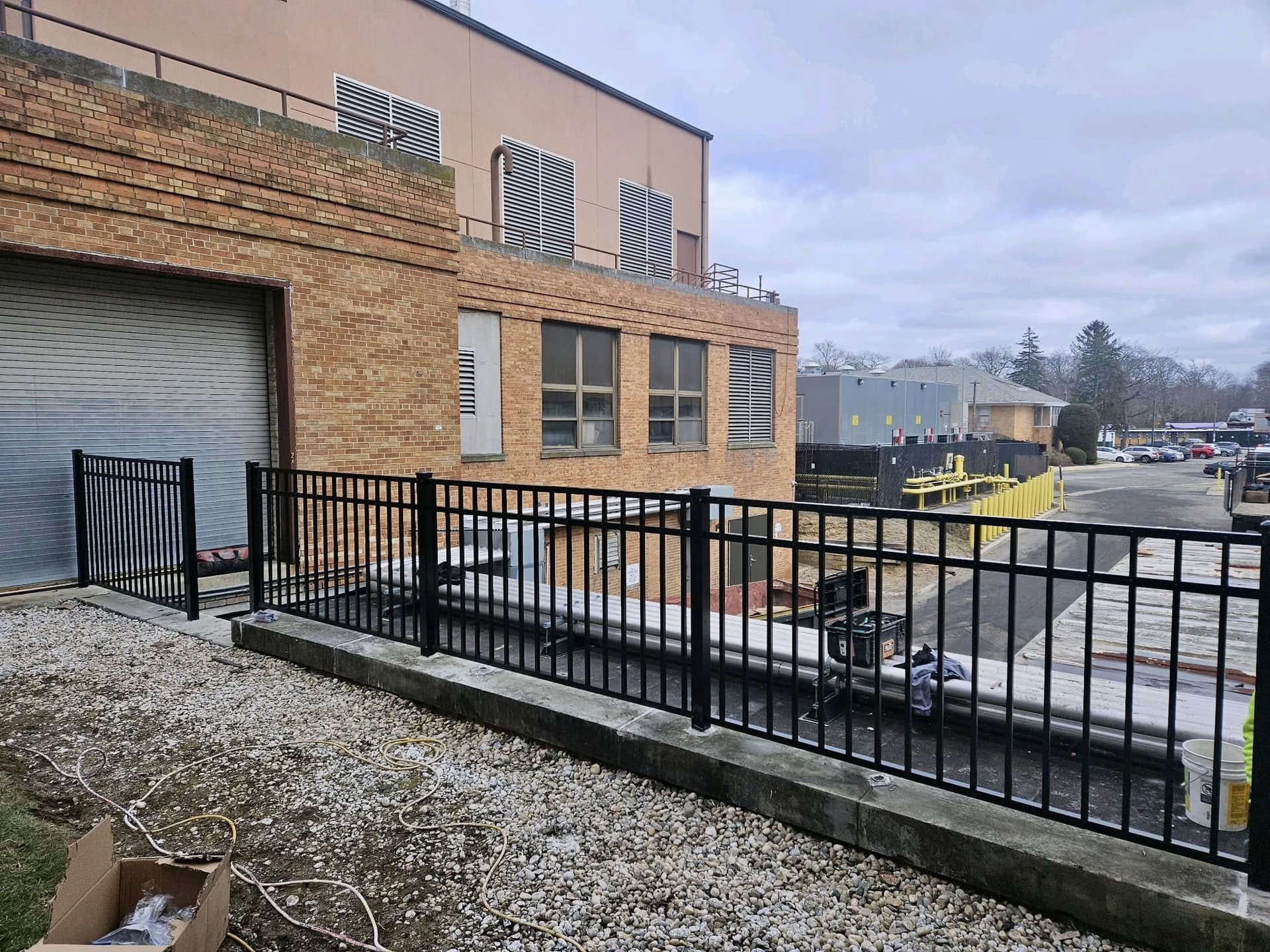 Black metal fence in front of a brick building. Gray sky.